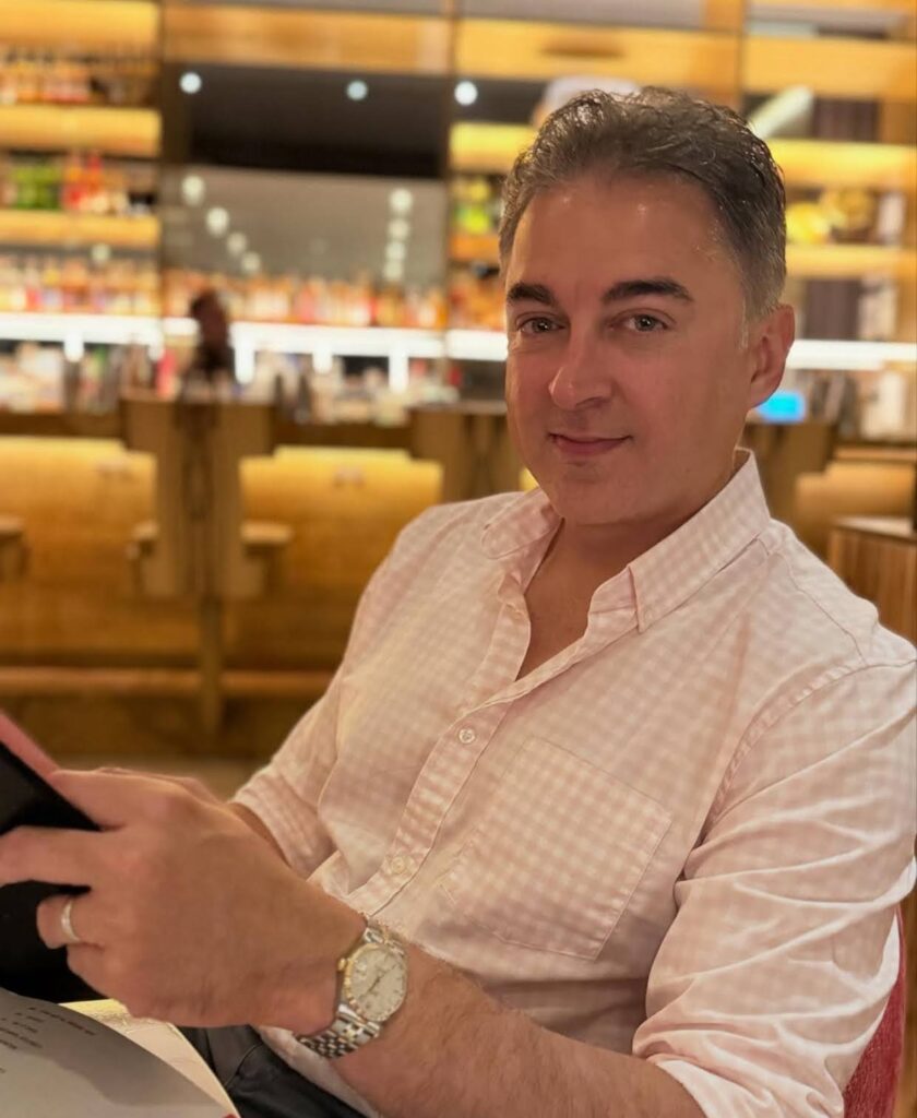 Jugal Hansraj wearing a light-colored shirt sitting indoors at a restaurant, holding a menu.