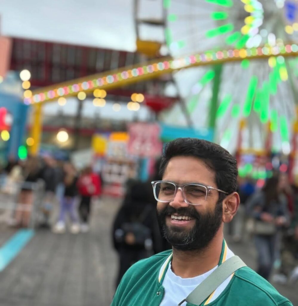 A cheerful moment captured at a vibrant amusement park with lights and a ferris wheel behind him.