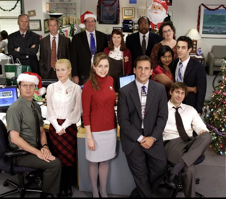 Cast of The Office posing together in a decorated office setting during a Christmas episode.